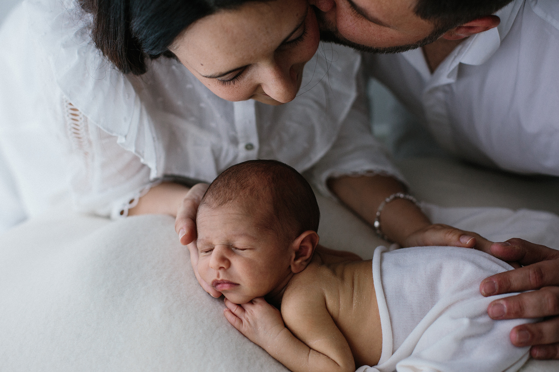 papà bacia la mamma che accarezza il neonato